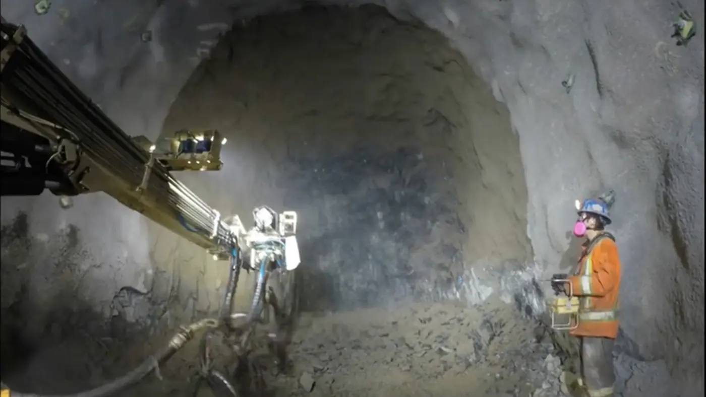 A shotcrete sprayer working in a drift with a crew member nearby.
