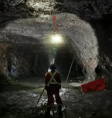 A miner with a cap lamp walking a wet drift.